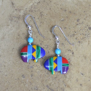 May include: A pair of silver earrings with turquoise beads and colorful geometric designs. The earrings are in the shape of a buffalo head.