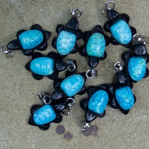May include: A group of ten turquoise turtle charms with black accents. The charms are arranged in a circle on a light brown surface. The text "Batch #5" is visible in the top left corner of the image.