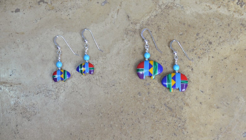 May include: A pair of silver earrings with turquoise beads and colorful geometric designs. The earrings are in the shape of a buffalo head.