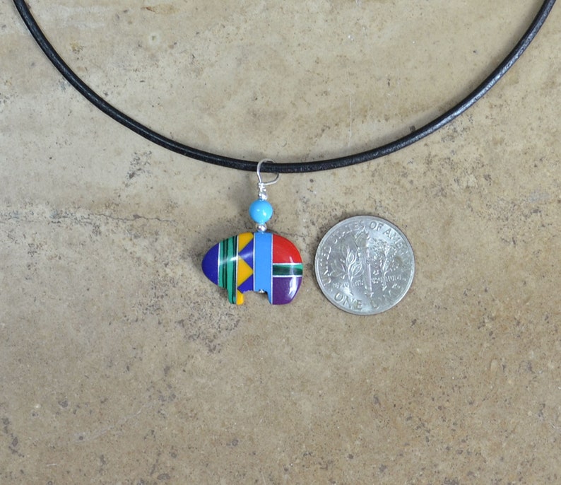 May include: A colorful Native American-style buffalo pendant necklace with a turquoise bead on a black leather cord. The pendant is about the size of a US quarter.