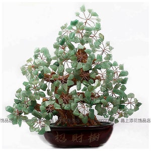 Puede incluir: Un árbol bonsái decorativo con hojas de piedras preciosas verdes y un tronco marrón. El árbol está en una maceta de cerámica marrón oscuro. La maceta tiene caracteres chinos. Es un artículo de decoración del hogar único.