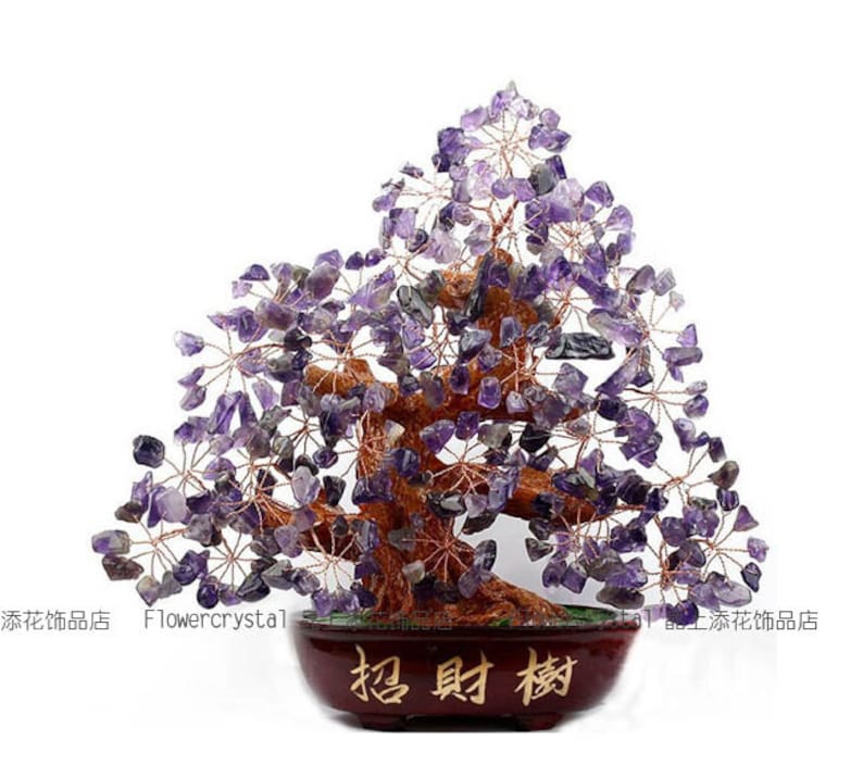 May include: A decorative amethyst crystal tree sculpture. The tree features a brown trunk and branches, with clusters of purple amethyst stones. The tree sits in a dark brown pot with Chinese characters. The words "Flowercrystal" are also visible.
