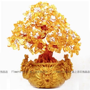Puede incluir: Una escultura decorativa de árbol con un dosel de piedras preciosas de color amarillo dorado. El tronco marrón se asienta en una maceta dorada adornada con motivos de dragones. Las palabras "Flowercryst" y caracteres chinos son visibles.