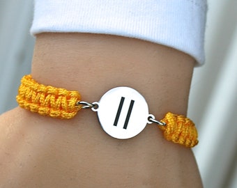 May include: A yellow braided bracelet with a silver round charm featuring two parallel lines.
