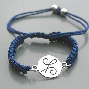 May include: Two blue friendship bracelets. One is a braided macrame style with a silver charm. The other is a simple cord bracelet with adjustable silver beads. Both bracelets are on a gray background.
