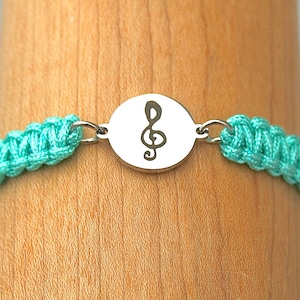 May include: A turquoise braided bracelet with a silver charm featuring a treble clef.