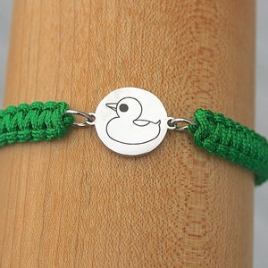 May include: A green braided bracelet with a silver charm featuring a rubber ducky design.