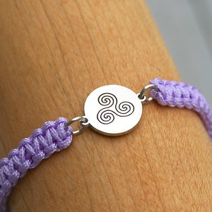May include: A purple braided bracelet with a silver charm featuring a Celtic knot design.