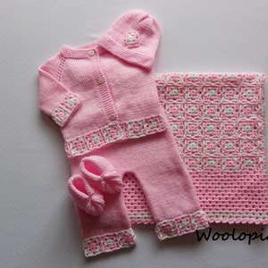 Puede incluir: Un conjunto de ropa de beb&eacute; de punto rosa con gorro, botines y manta a juego. El conjunto presenta ribetes de ganchillo blanco y un cierre de bot&oacute;n en el c&aacute;rdigan.