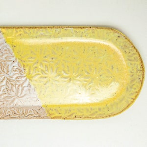 Puede incluir: Un plato de servir de cerámica amarillo y blanco con un diseño floral. El plato tiene forma ovalada y un acabado brillante.