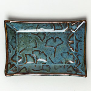 Könnte beinhalten: Rechteckige Keramikschale mit türkisfarbener Glasur und geprägtem Ginkgoblatt-Design. Die Ränder sind dunkelbraun umrandet. Die Schale ist ein dekorativer Artikel für das Zuhause.