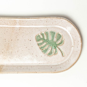 May include: A white ceramic oval serving tray with a green leaf design. The tray has a textured surface with a repeating pattern of circles.