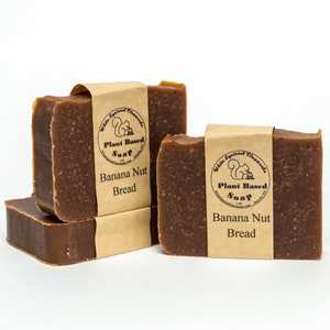Może przedstawiać: Dwa brązowe kawałki mydła roślinnego z brązową papierową etykietą z napisem "White Squirrel Claymarks Plant Based Soap Banana Nut Bread".