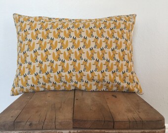 May include: A yellow and white throw pillow with a repeating pattern of orange foxes. The pillow is sitting on a wooden stool.