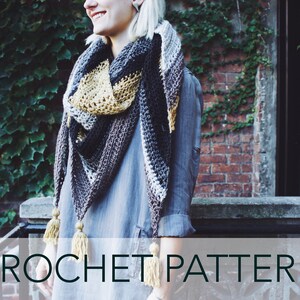 May include: A woman wearing a gray shirt and a crocheted shawl with brown, white, and yellow stripes. The shawl has tassels on the ends. CROCHET PATTERN is written in white text on a gray background.