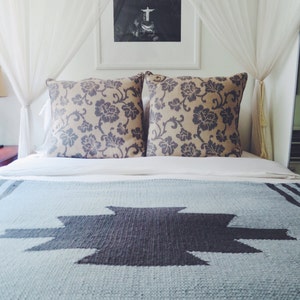 Puede incluir: Una cama con dosel blanco y una manta con estampado azul y gris. La cama tiene dos almohadas con estampado floral.
