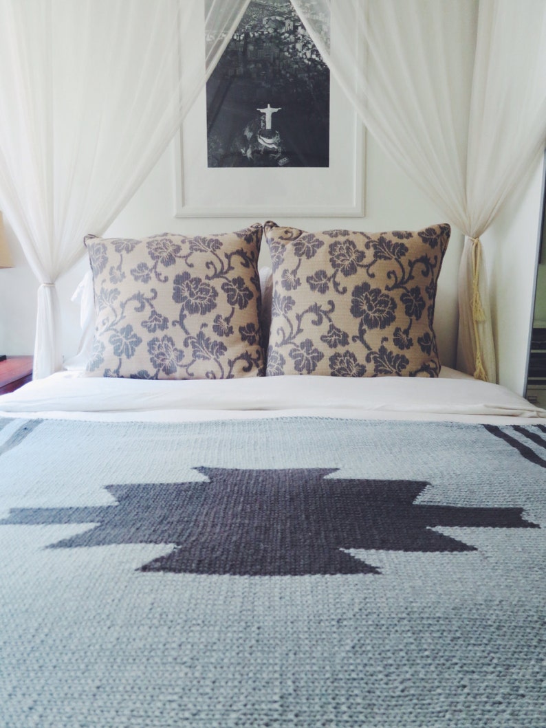 Puede incluir: Una cama con dosel blanco y una manta con estampado azul y gris. La cama tiene dos almohadas con estampado floral.