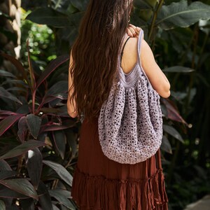 May include: A woman wearing a brown dress with a crocheted purple tote bag.