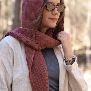 K&ouml;nnte beinhalten: Eine Frau tr&auml;gt einen Kapuzen-Schal in einem tiefen Rosaton. Der Schal ist gestrickt und hat einen lockeren, flie&szlig;enden Stil. Sie tr&auml;gt auch eine hellbeige Jacke und ein graues Hemd.