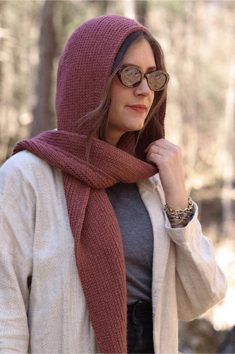 K&ouml;nnte beinhalten: Eine Frau tr&auml;gt einen Kapuzen-Schal in einem tiefen Rosaton. Der Schal ist gestrickt und hat einen lockeren, flie&szlig;enden Stil. Sie tr&auml;gt auch eine hellbeige Jacke und ein graues Hemd.