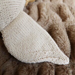 May include: Close-up of a knitted, off-white fabric, possibly a stuffed animal's ear or foot, resting on a brown, faux fur blanket. The knitted piece has a rounded shape and a textured surface.