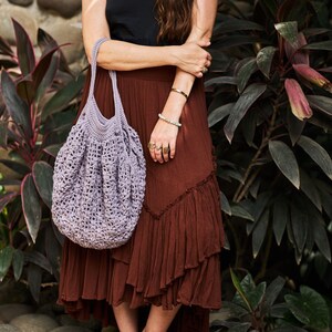 May include: A woman wearing a brown skirt and a black tank top is holding a purple crocheted tote bag.