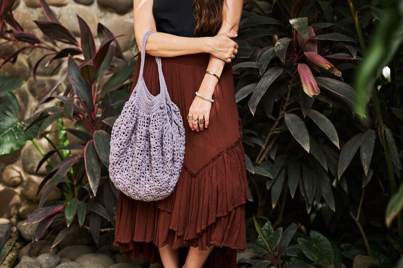 May include: A woman wearing a brown skirt and a black tank top is holding a purple crocheted tote bag.