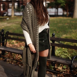 May include: A woman wearing a green knitted scarf, a white sweater, a green corduroy skirt, and green thigh-high socks. She is standing in front of a wooden bench.