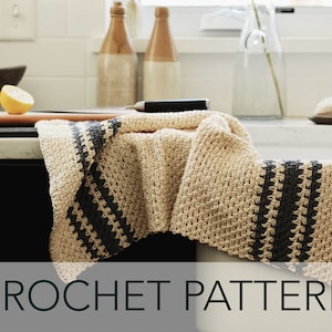May include: A crocheted kitchen towel with black and beige stripes. The towel is folded and draped over a kitchen counter.