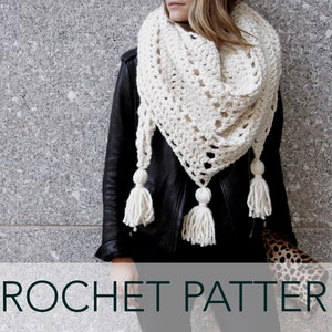 Puede incluir: Un chal de crochet blanco con un patrón de encaje y borlas. El chal está drapeado sobre una persona que lleva una chaqueta de cuero negra.