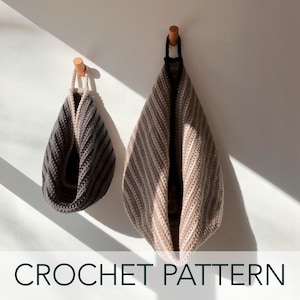 Può includere: Due borse all'uncinetto appese a ganci. La borsa più grande è beige e marrone con un motivo a righe. La borsa più piccola è grigio scuro e bianco con un motivo a righe. CROCHET PATTERN è scritto in nero nella parte inferiore dell'immagine.