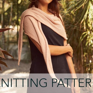 May include: A knitting pattern for a light pink triangular scarf. The scarf is draped around a person's neck and shoulders. The background is a blurred image of green foliage.