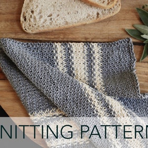 May include: Knitting pattern for a striped dishcloth in blue and cream. The dishcloth is folded and lying on a wooden surface with bread and herbs.