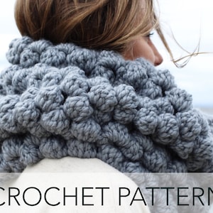 May include: A grey crocheted cowl neck scarf with a textured, puffy design. CROCHET PATTERN is written in black text at the bottom of the image.