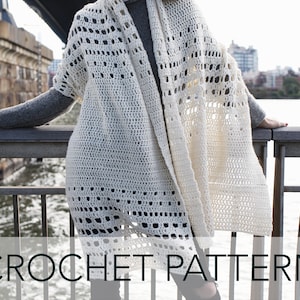 May include: Cream-colored crochet shawl with openwork design. The shawl is draped over a person wearing a gray turtleneck. The text "CROCHET PATTERN" is at the bottom of the image. The background includes a bridge and city skyline.