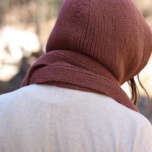 K&ouml;nnte beinhalten: Nahaufnahme einer gestrickten Kapuzen-Schals in einem tiefen Rosaton. Der Schal ist aus weichem, dickem Garn gefertigt und hat ein schlichtes, klassisches Design.