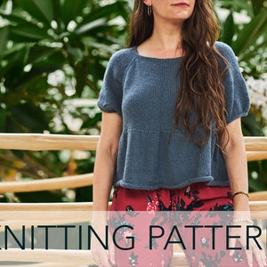 May include: Knitting pattern for a blue, short-sleeved top with a square neckline. The top is loose-fitting and has a slightly gathered hem. The model is wearing the top with red floral trousers.