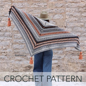 Puede incluir: Un patrón de crochet para una chal gris, negro y naranja con borlas. La chal está drapeada sobre los hombros de una persona.