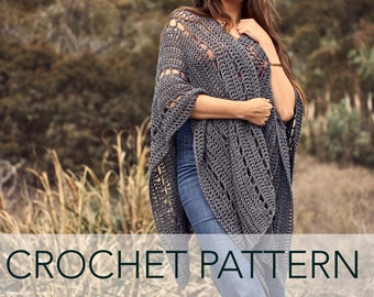 May include: A gray crochet poncho with a lacy pattern. The poncho is worn by a person standing in a field of tall grass.