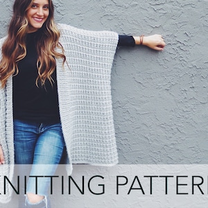 May include: A woman wearing a gray knitted cardigan with a waffle stitch pattern. The cardigan is open in the front and has long sleeves. The woman is standing in front of a gray wall. The text "KNITTING PATTERN" is at the bottom of the image.