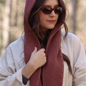 K&ouml;nnte beinhalten: Eine Frau tr&auml;gt einen Kapuzen-Schal in einem tiefen Rosaton. Der Schal ist gestrickt und hat ein strukturiertes Muster. Sie tr&auml;gt einen hellbeigen Pullover und eine braune Sonnenbrille.