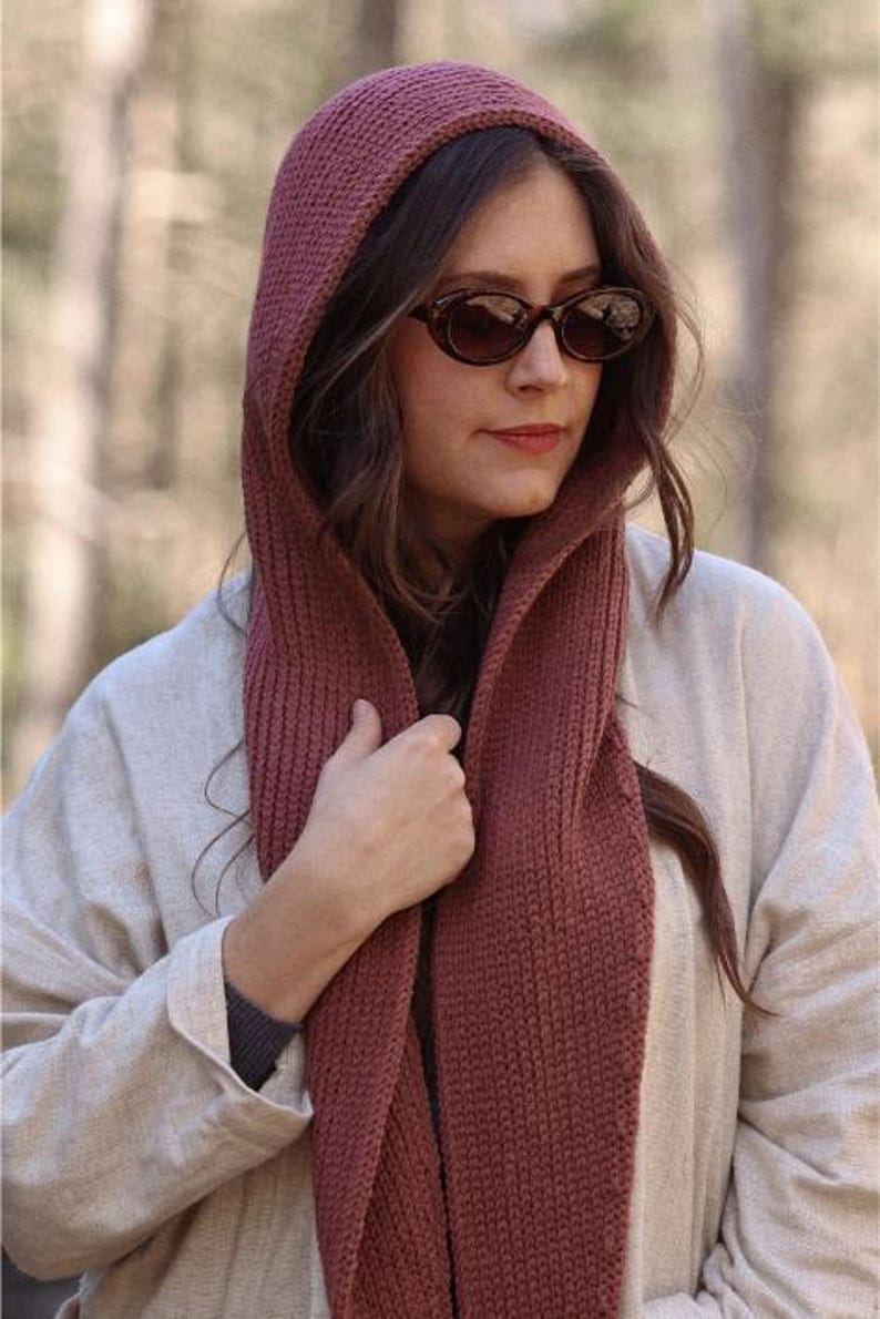 K&ouml;nnte beinhalten: Eine Frau tr&auml;gt einen Kapuzen-Schal in einem tiefen Rosaton. Der Schal ist gestrickt und hat ein strukturiertes Muster. Sie tr&auml;gt einen hellbeigen Pullover und eine braune Sonnenbrille.