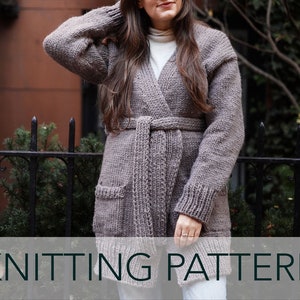 Puede incluir: Un cárdigan de punto con estilo de envoltura y cinturón. El cárdigan es de color marrón claro y tiene bolsillos. El cárdigan lo lleva puesto una persona delante de una pared de ladrillo y una valla de metal negra.