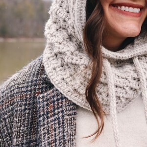 May include: A close-up of a person wearing a white crocheted hooded cowl with a drawstring. The cowl is worn over a white sweater and a plaid jacket.