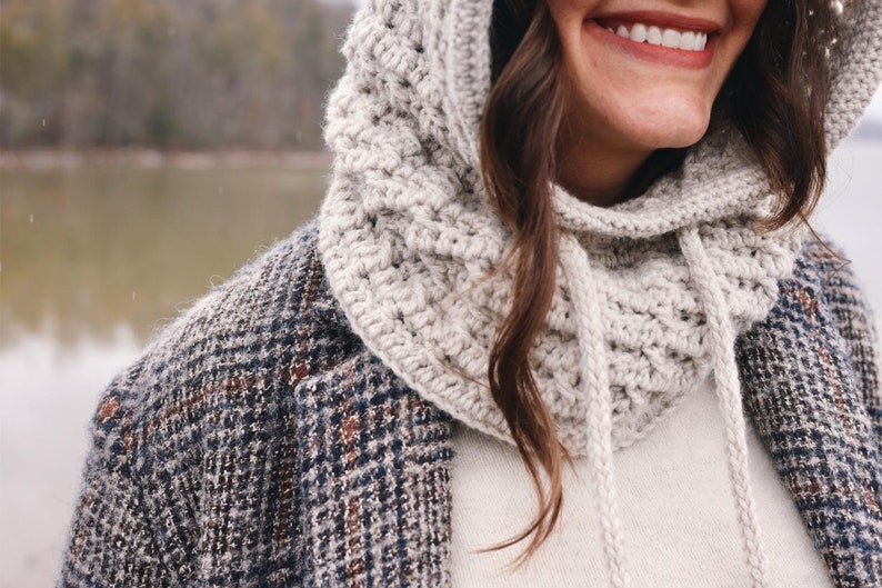 May include: A close-up of a person wearing a white crocheted hooded cowl with a drawstring. The cowl is worn over a white sweater and a plaid jacket.