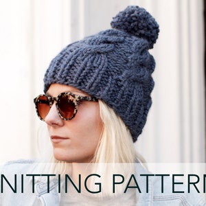 May include: A blue knitted beanie with a cable knit pattern and a fluffy pom pom on top. The beanie is worn by a person with blonde hair and sunglasses. The text "KNITTING PATTERN" is displayed below the image.