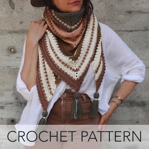 Puede incluir: Un chal de ganchillo de forma triangular, con rayas en tonos marrón, crema y rosa. El chal tiene borlas en los extremos y el texto "CROCHET PATTERN" en la parte inferior.