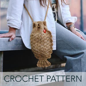 May include: A tan crochet fish-shaped bag with a drawstring closure and a red button. The bag has a long strap and is worn over the shoulder. The words "CROCHET PATTERN" are at the bottom of the image.