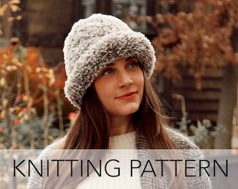 Puede incluir: Primer plano de una mujer con un gorro de punto gris y marrón peludo. El gorro tiene un ala ancha y está doblado sobre las orejas. El gorro es un patrón de punto.