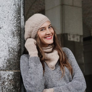 Puede incluir: Una mujer con un su&eacute;ter de punto gris, un gorro de punto beige y una bufanda de punto beige. Est&aacute; sonriendo y mirando hacia la derecha.